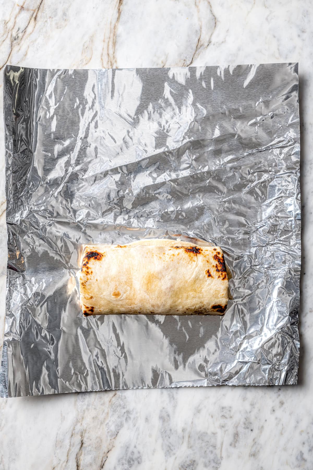These easy freezer breakfast burritos are a delicious, protein-packed way to start the day with scrambled eggs, veggies, bacon and cheese. Breakfast burrito on foil