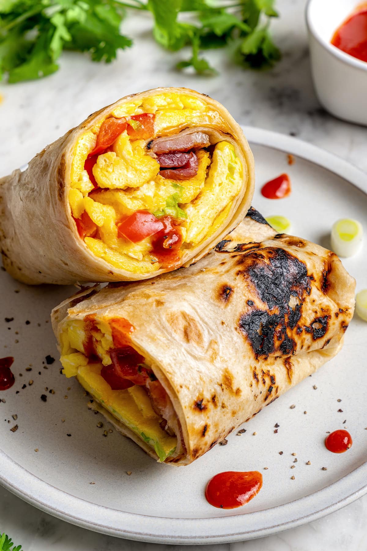 These easy freezer breakfast burritos are a delicious, protein-packed way to start the day with scrambled eggs, veggies, bacon and cheese. Freezer breakfast burrito cut in half on plate