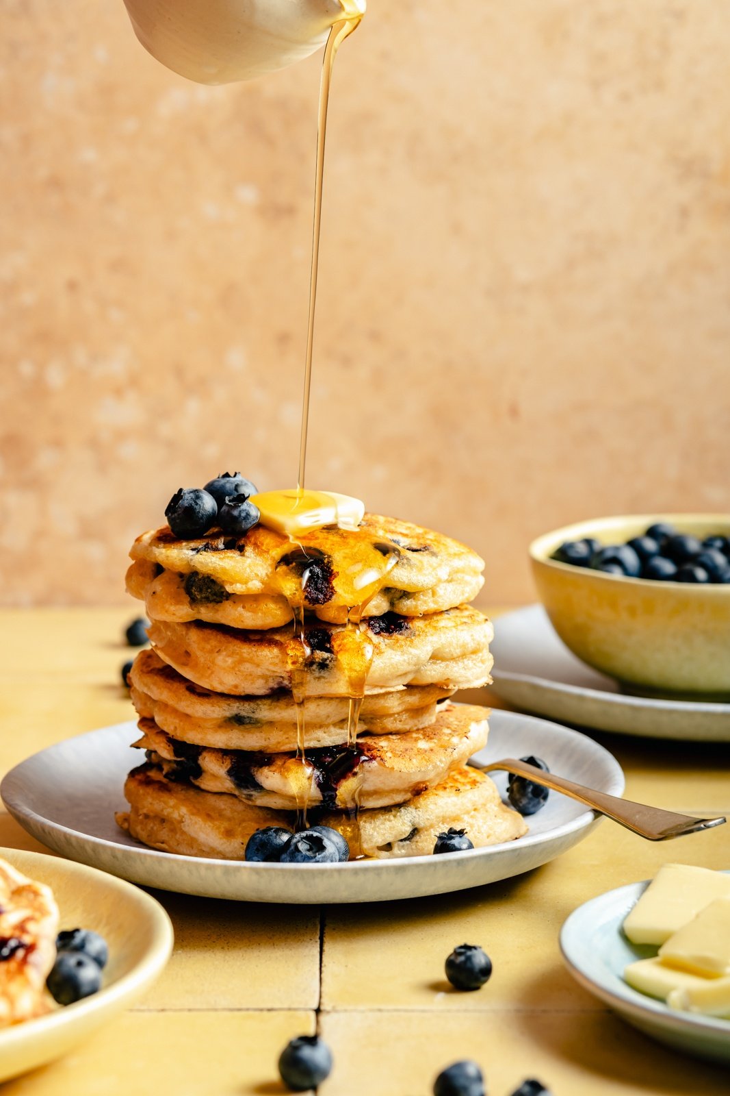 drizzling syrup onto a stack of blueberry buttermilk pancakes