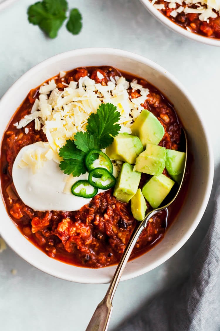 healthy pumpkin turkey chili in a bowl with a spoon topped with avocado