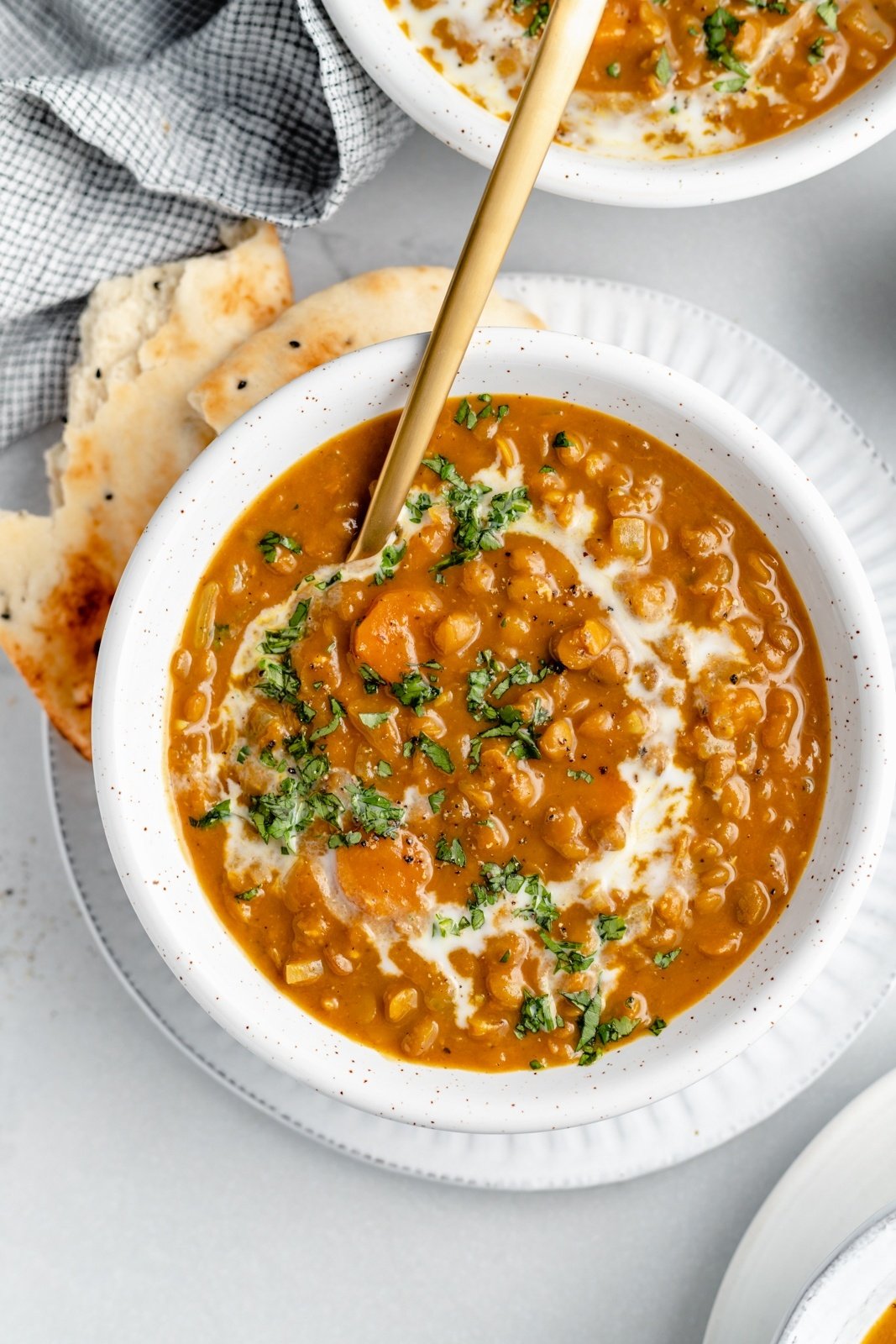 vegan pumpkin lentil soup in a bowl with a spoon and naan