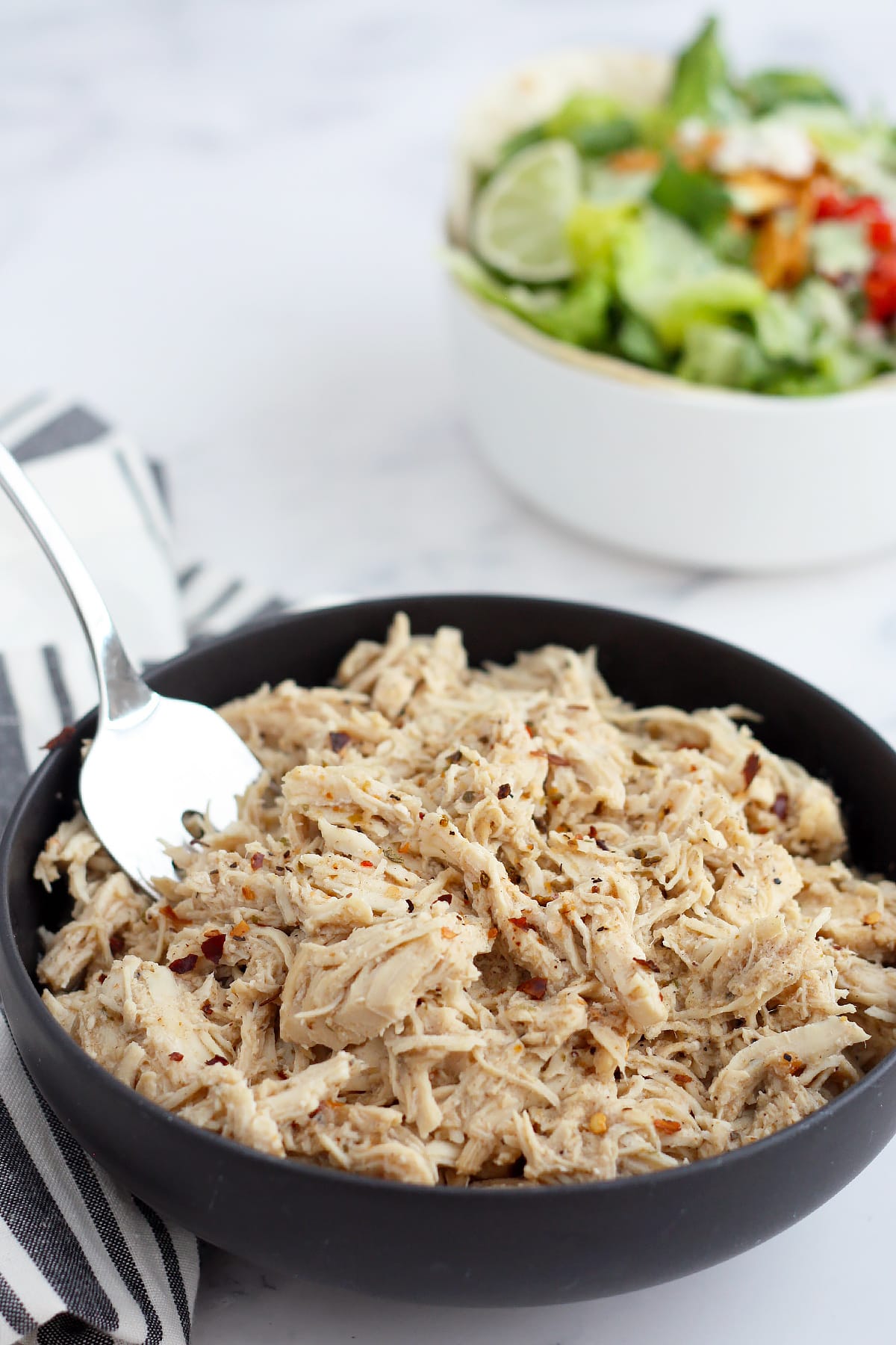 shredded  chicken in a bowl with spices and a salad in the background