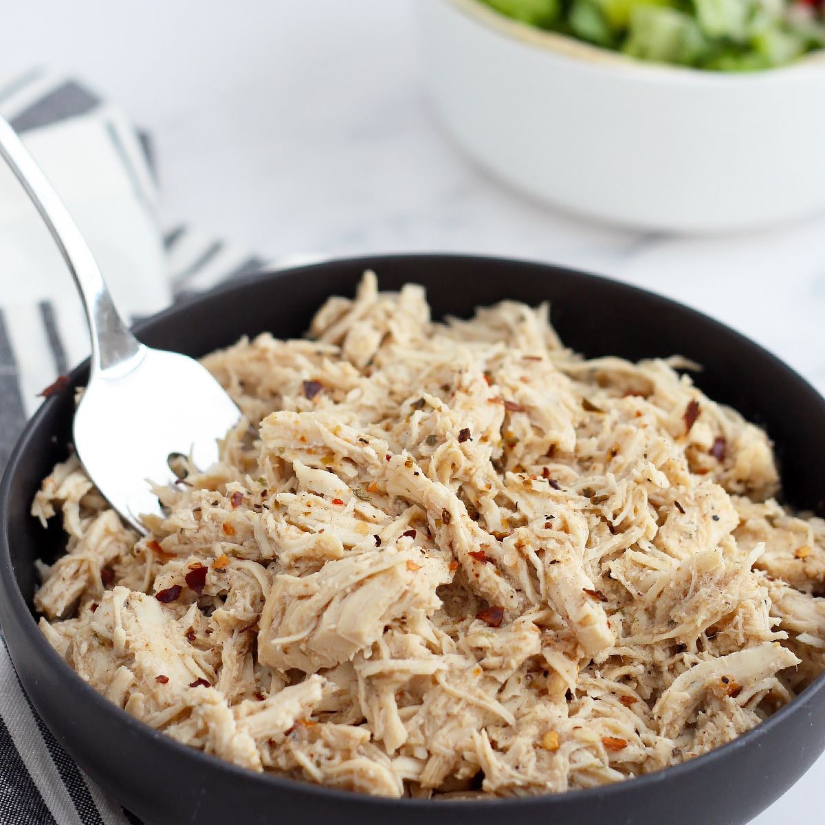 cafe rio shredded  chicken in a bowl with spices and a salad in the background