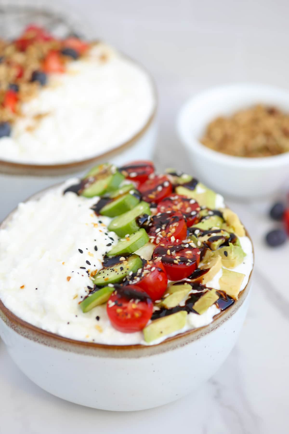 a close up view of a bowl of cottage cheese with savory ingredients on top