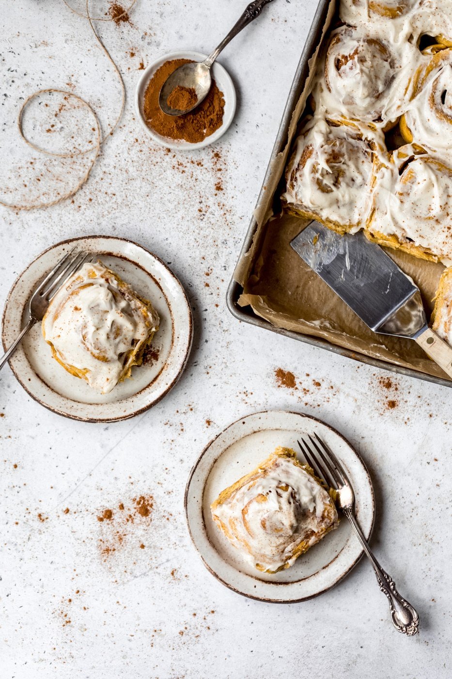 pumpkin cinnamon rolls on two plates with forks and a pan on the side