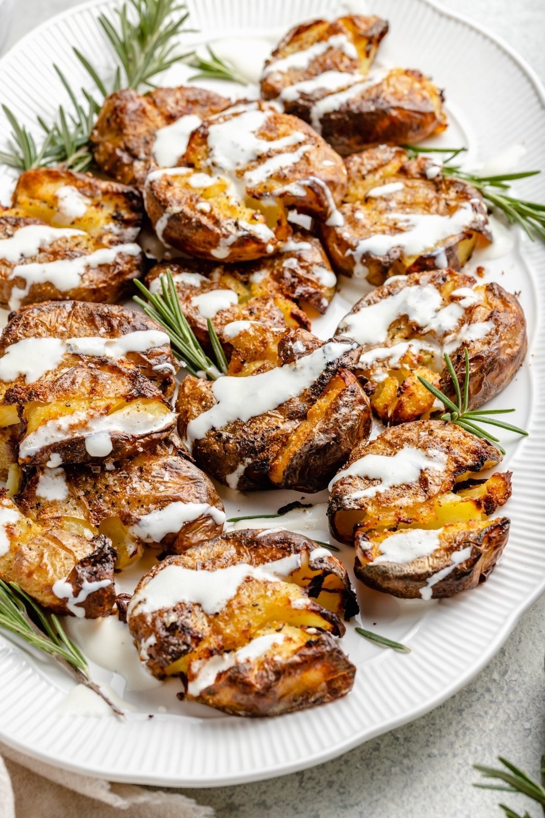 crispy smashed potatoes on a platter drizzled in feta sauce