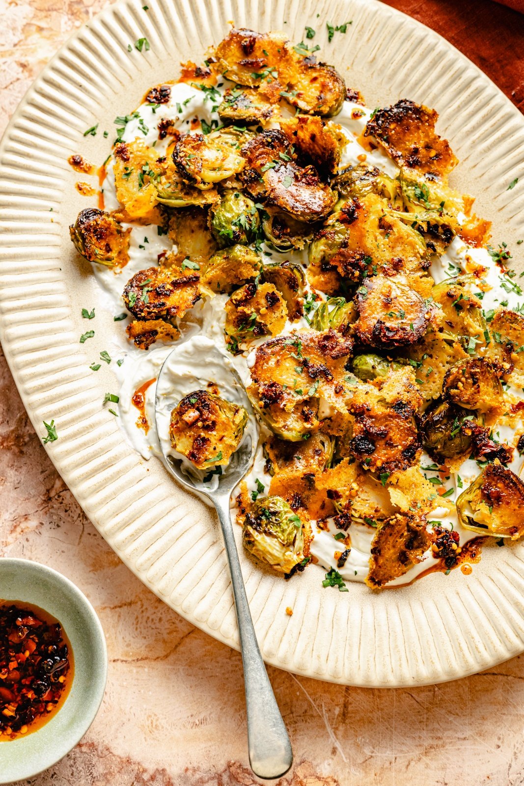 spicy roasted brussels sprouts with parmesan cheese on a platter with tahini yogurt sauce