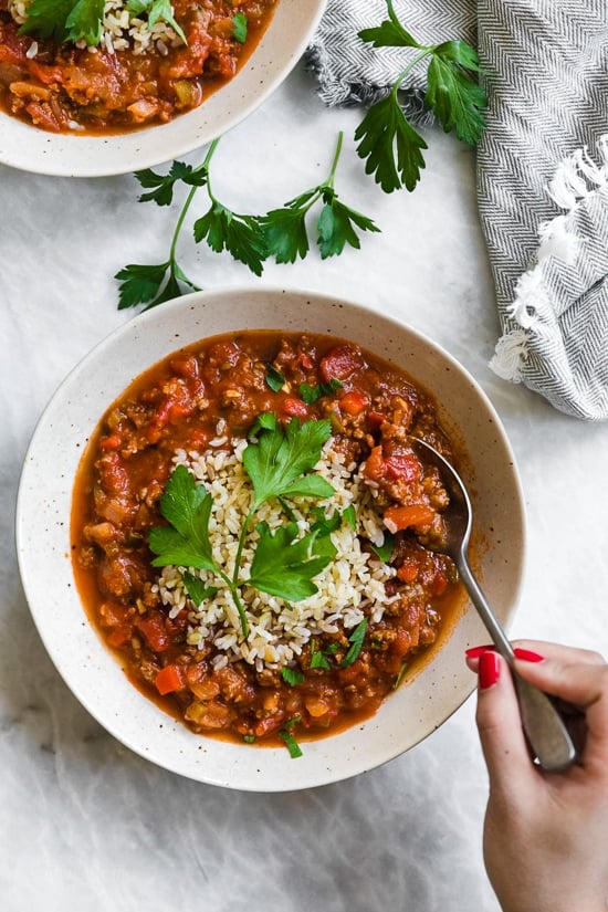 This easy stuffed pepper soup has bell peppers, ground beef, tomatoes, and rice in a hearty bowl of soup. Stovetop and Instant Pot options! Hand digging into bowl of stuffed pepper soup