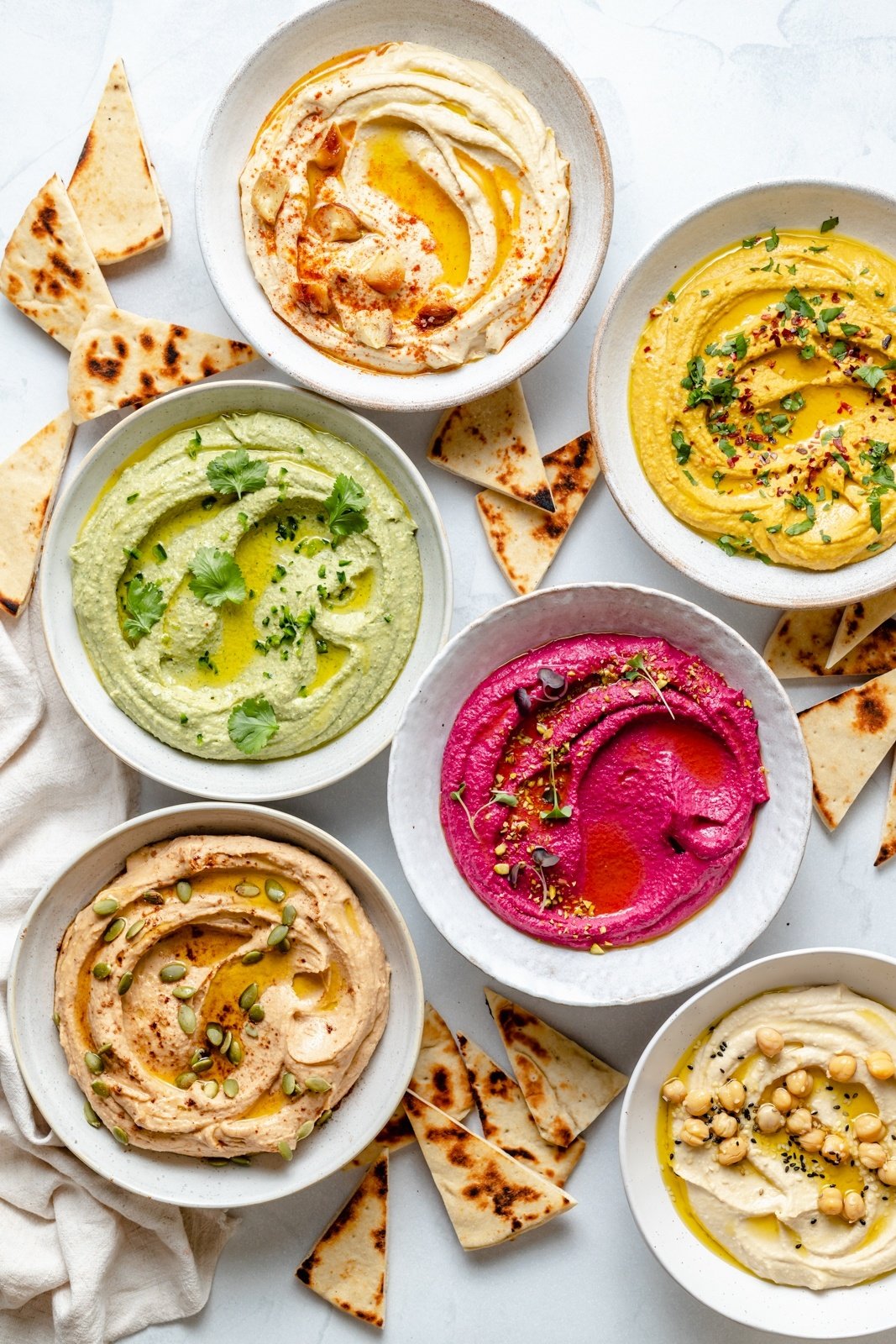 five bowls of homemade hummus on a board