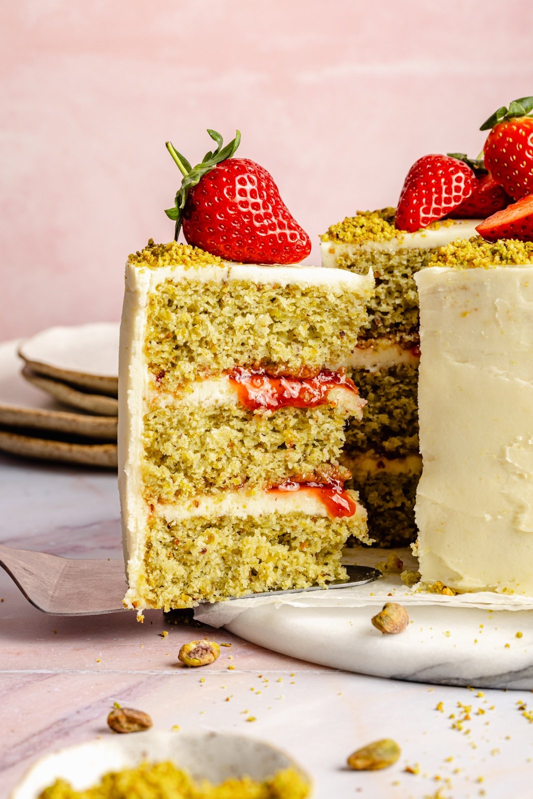 pulling a slice of lemon pistachio cake out from the full cake