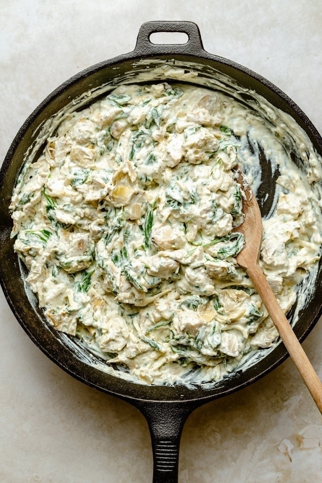 mixing ingredients for spinach artichoke dip with fresh spinach in a skillet