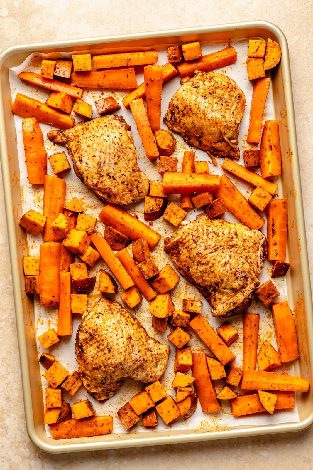unbaked chicken, sweet potatoes and carrots on a sheet pan