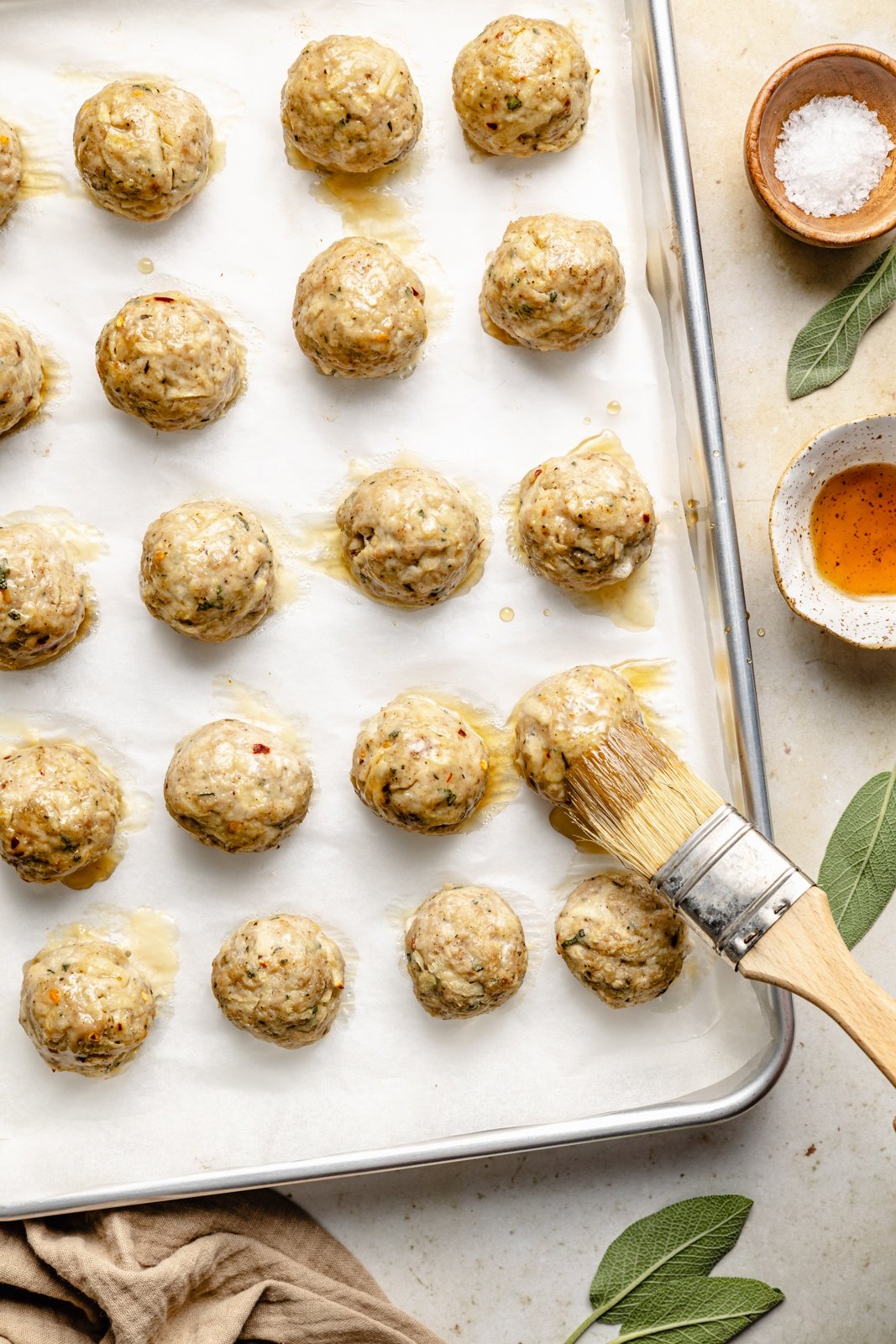brushing chicken breakfast meatballs on a baking sheet with maple syrup