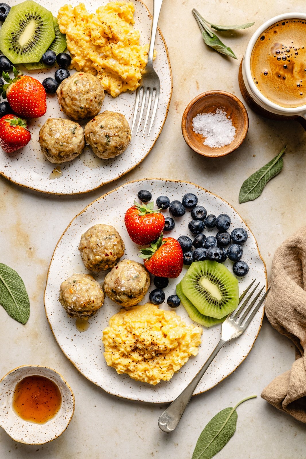 two plates with chicken breakfast meatballs, eggs, and fresh fruit