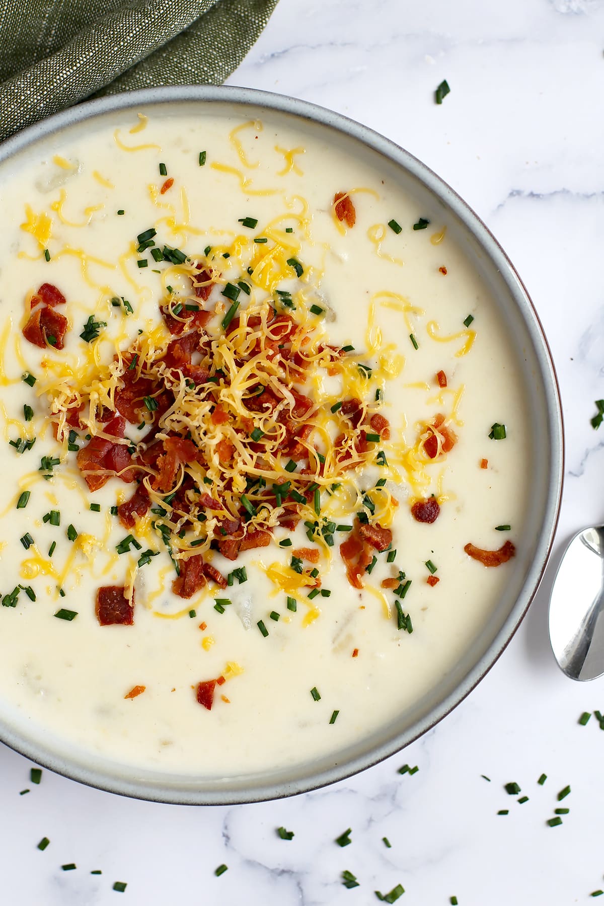 A close up image of a bowl of loaded baked potato soup with onions, bacon and cheese.