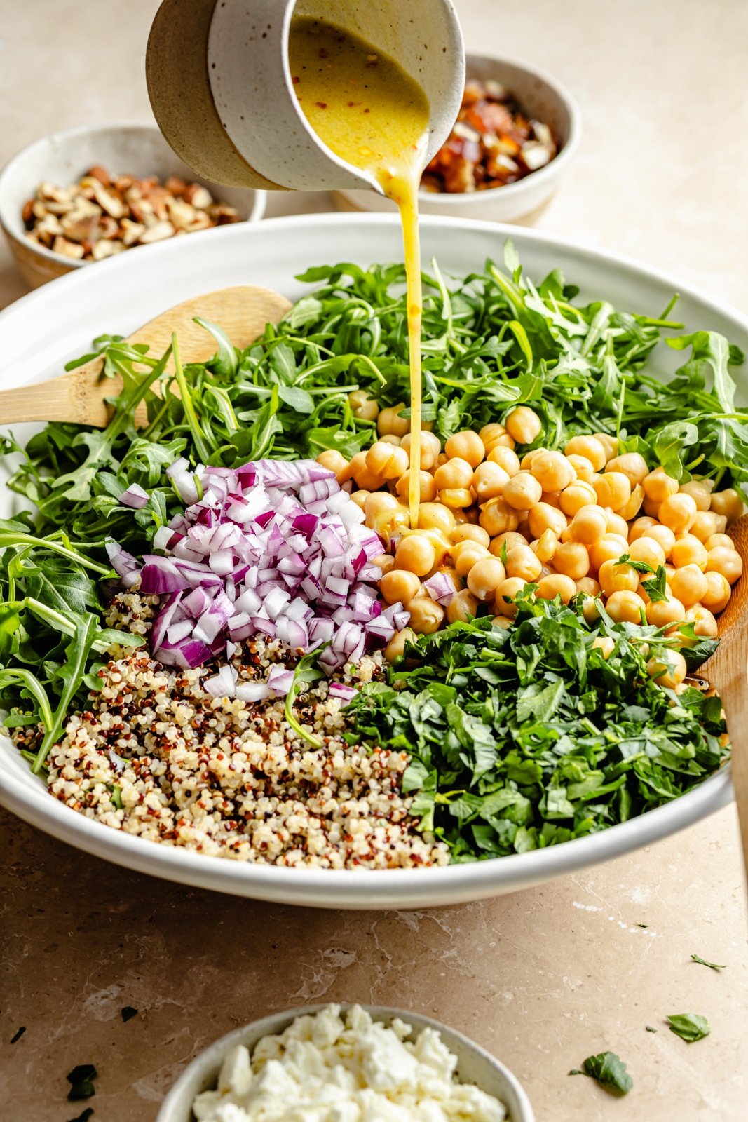 pouring dressing onto an arugula quinoa salad with chickpeas