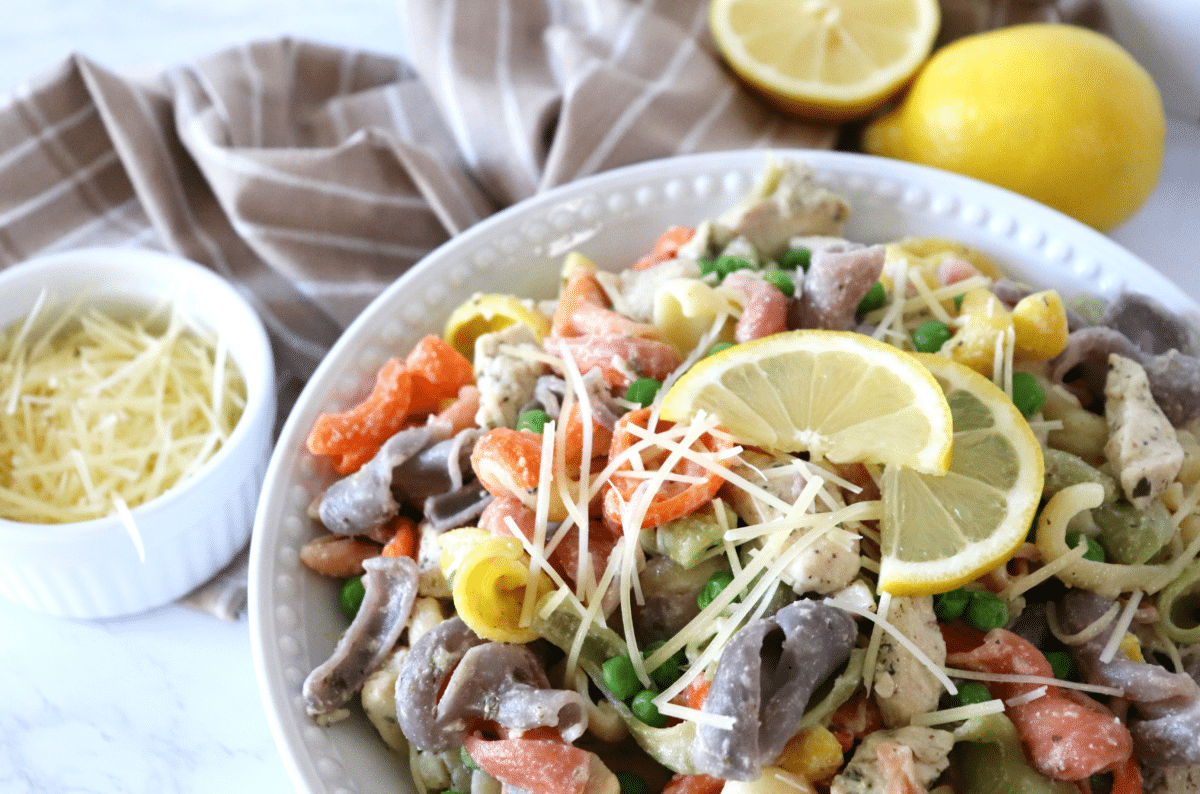 Lemon pasta with chicken in a white serving bowl and topped with shredded parmesan and lemon slices.