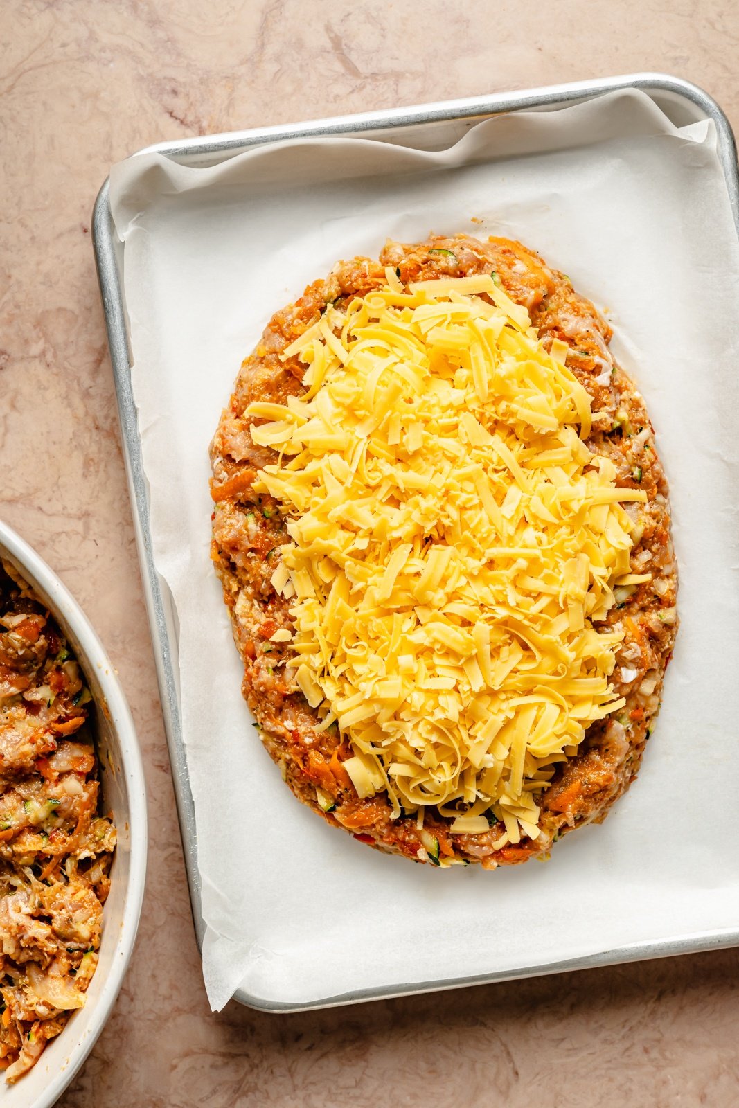 unbaked chicken meatloaf on a pan topped with cheese