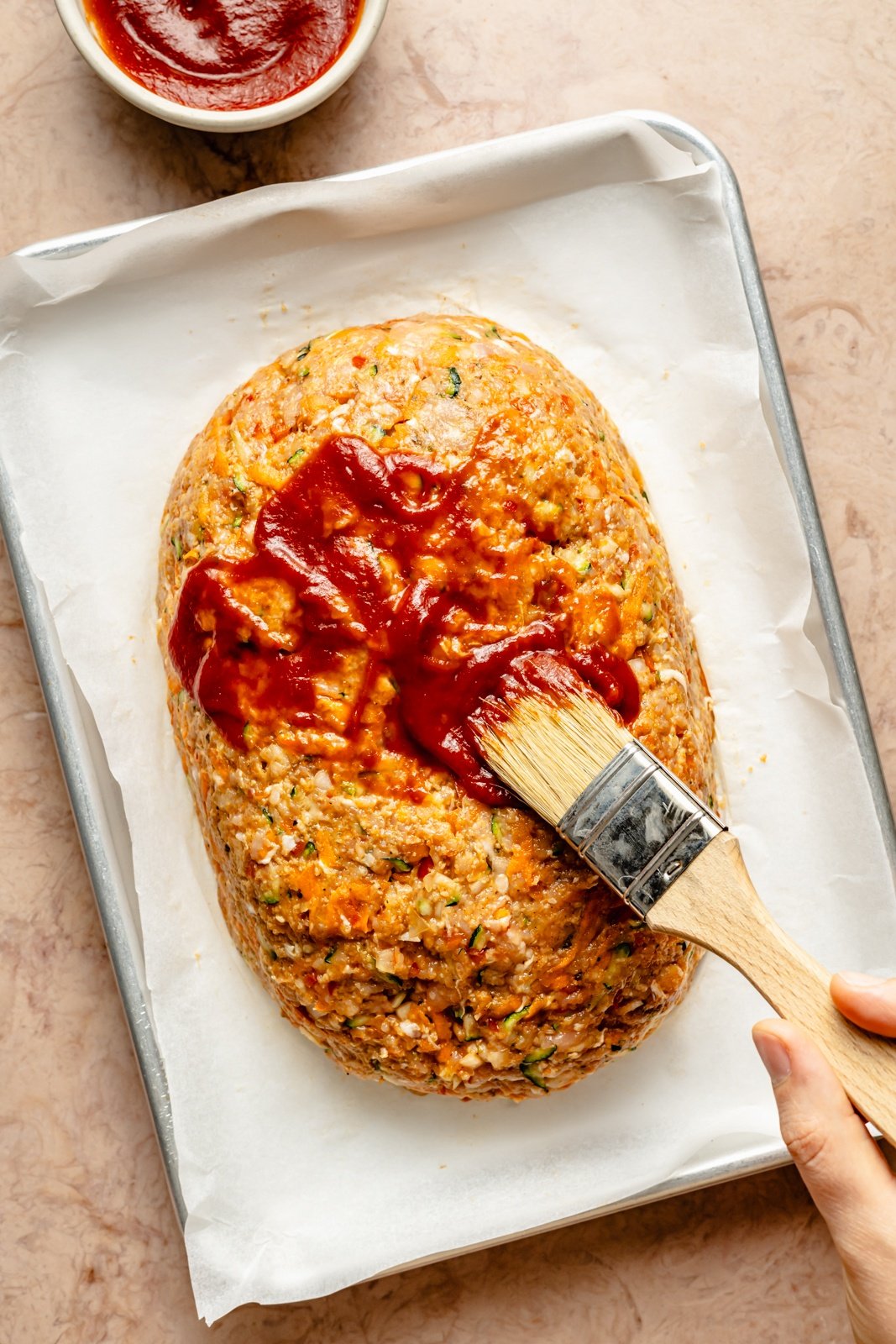 brushing an unbaked chicken meatloaf with ketchup