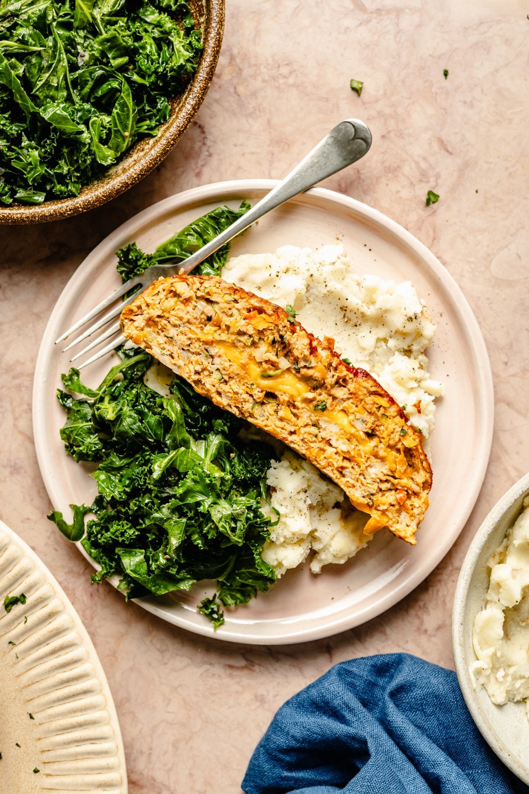 slice of veggie-packed chicken meatloaf on a plate with salad an mashed potatoes
