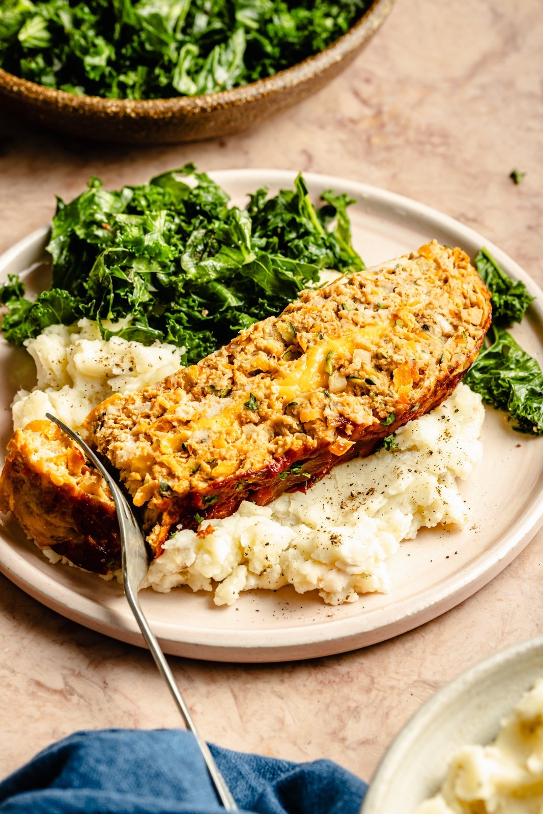 slice of veggie-packed chicken meatloaf on a plate with mashed potatoes and salad