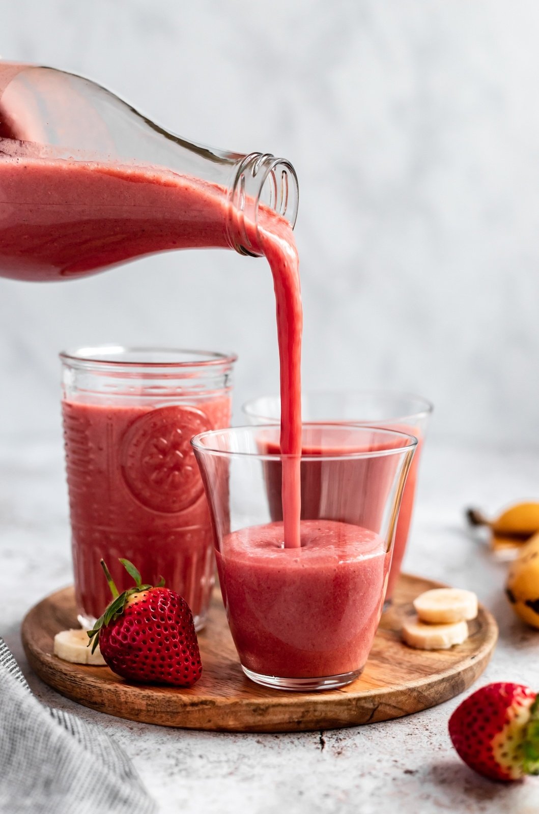 pouring a strawberry orange banana smoothie into a glass