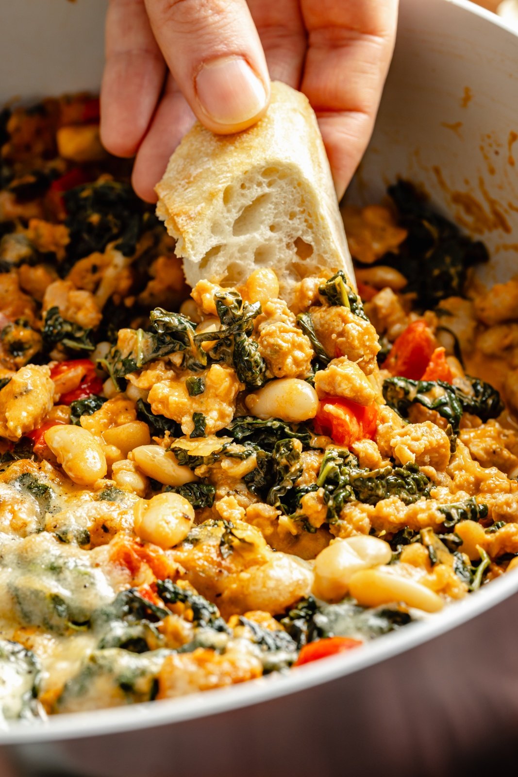 scooping kale and sausage white bean bake from a skillet with bread