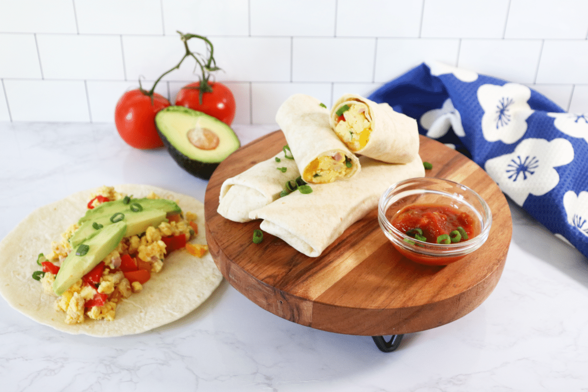 Breakfast burritos on a wooden stand with a side of salsa.