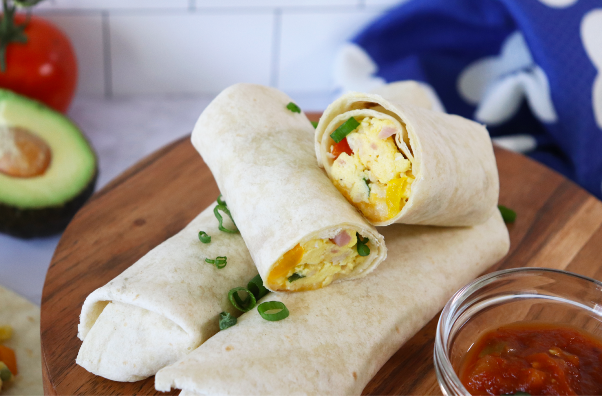 Breakfast burritos with eggs, veggies, and ham piled on a wooden plate.