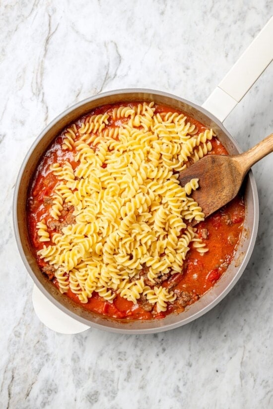 With ground beef, tomatoes, pickles, and cheese, this lightened up cheeseburger casserole recipe is kid-friendly and so delicious! Overhead view of pasta added to ground beef mixture