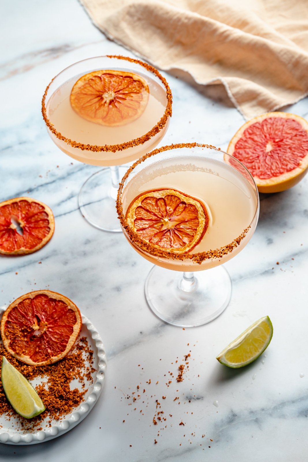 two grapefruit margaritas in glasses next to dried grapefruit slices