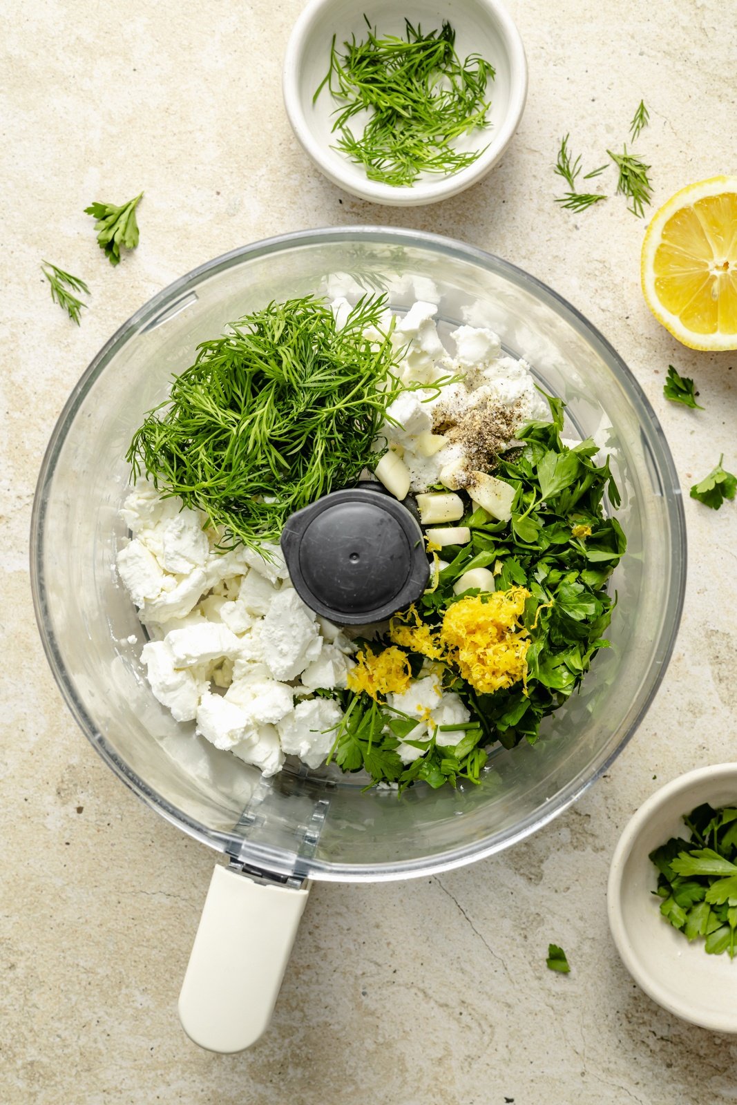 ingredients for a creamy herbed goat cheese spread in the bowl of a food processor