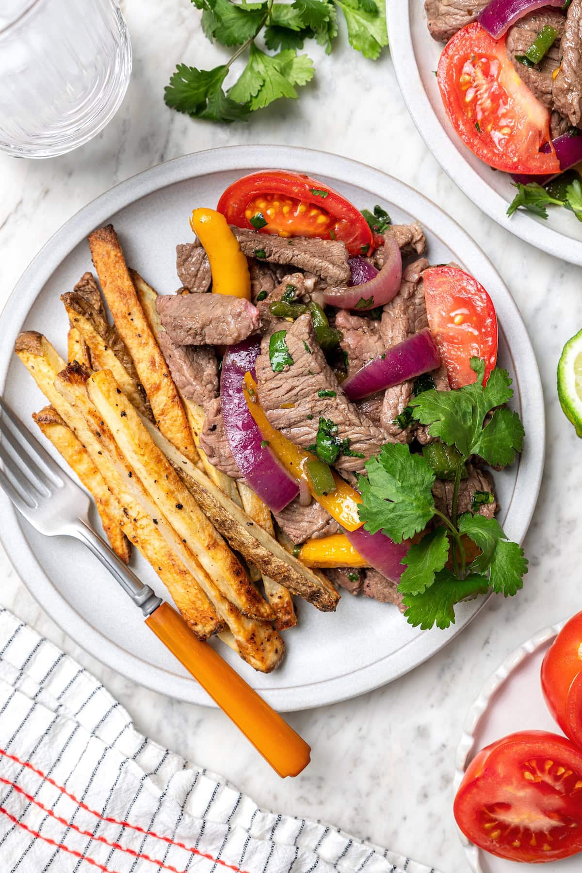 This lightened up Peruvian lomo saltado recipe is packed with flavor, with tender sirloin and veggies served alongside crispy baked fries. Peruvian lomo saltado on plate with fork and sprig of cilantro
