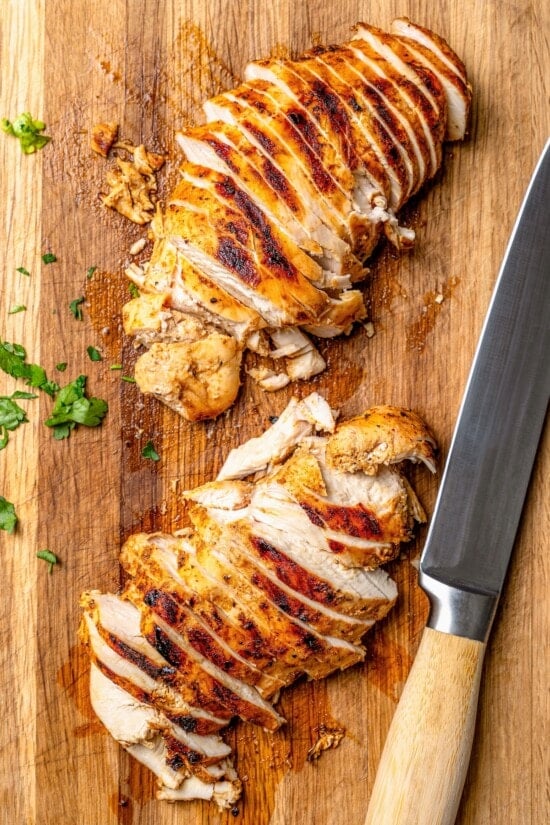 These easy chicken fajitas are made with grilled chicken breast, bell peppers and onions and served sizzling hot with tortillas and cheese! Overhead view of sliced chicken on cutting board with knife