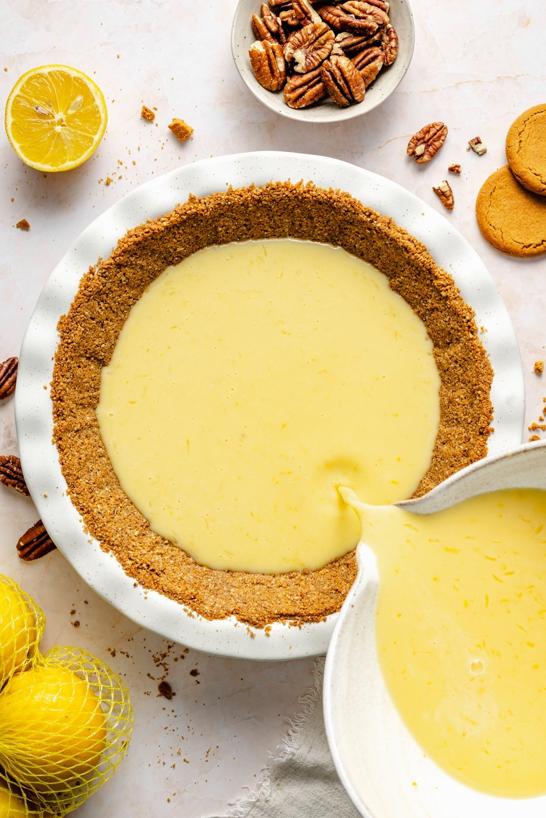 pouring lemon cream pie filling into a pecan gingersnap cookie crust