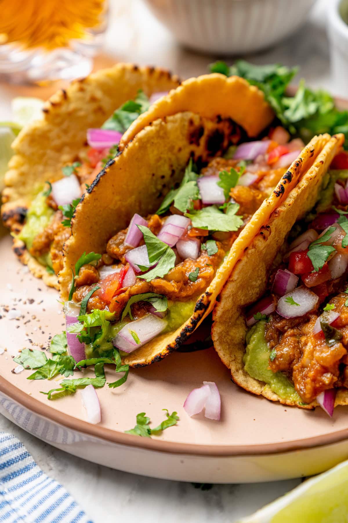 These vegan lentil tacos are easy to make, full of big Tex-Mex flavor and great for meal prep. Add your favorite toppings and dig in! Plate with 3 lentil tacos topped with cilantro and red onion