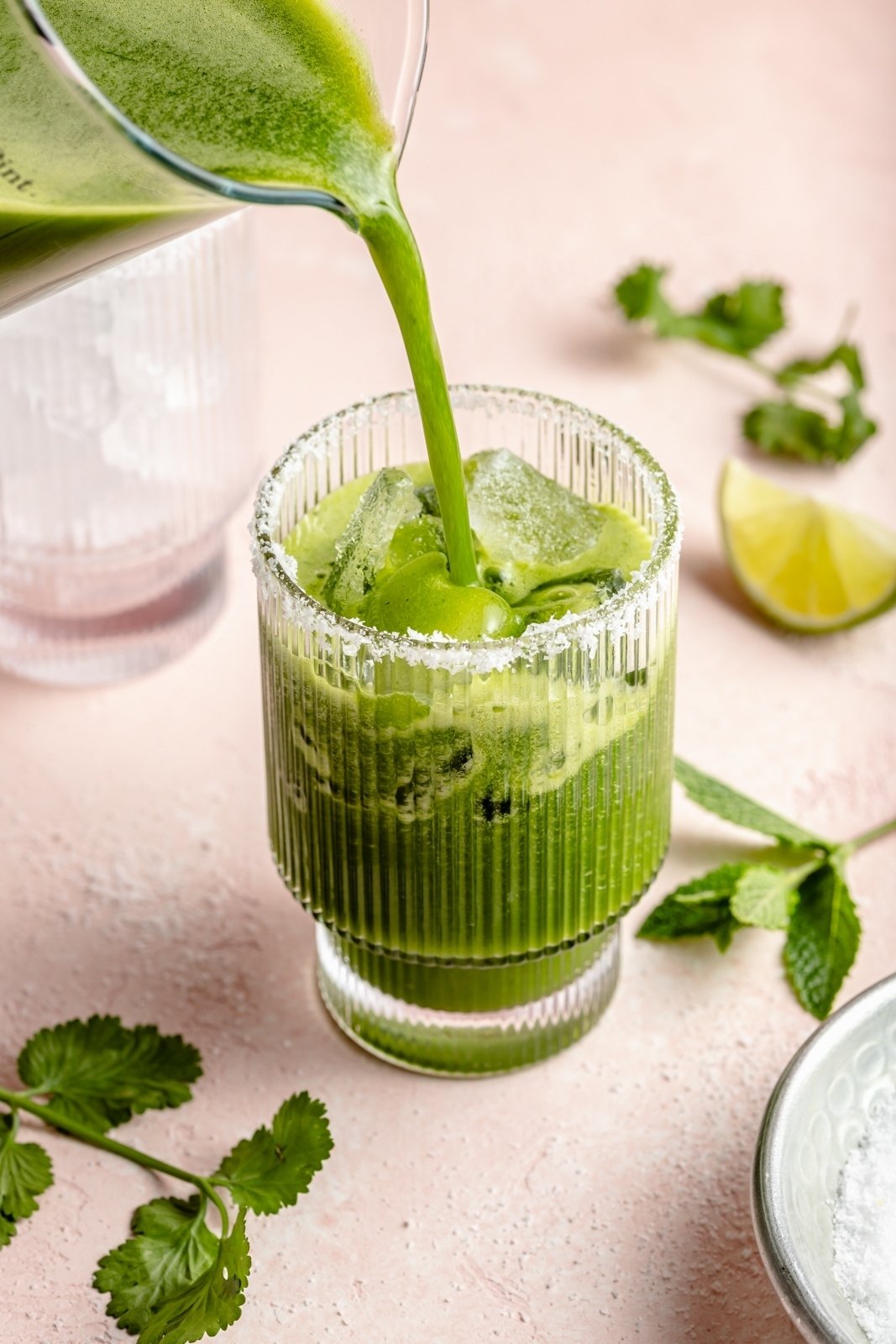 pouring a green juice cocktail into a glass