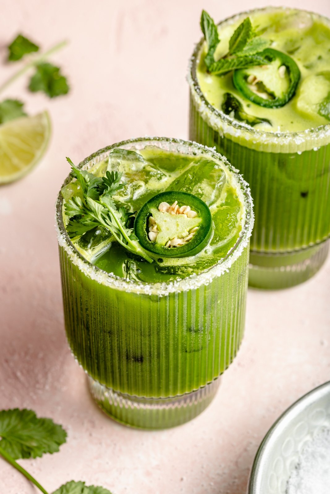 green margarita in a glass topped with herbs and a jalapeño slice