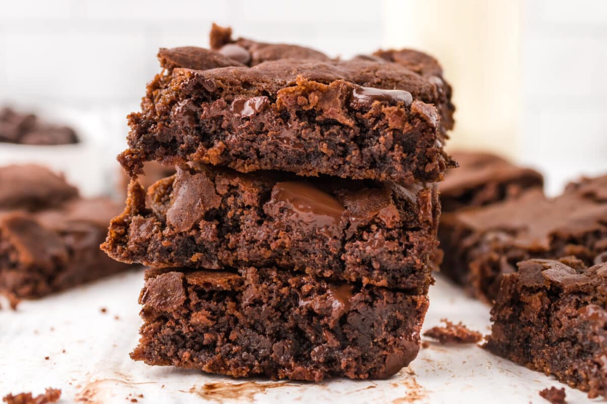 A stack of gooey chocolate chip brownies on parchment paper.