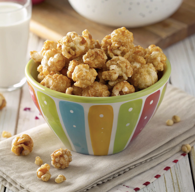 Susan's caramel corn in a serving bowl on a wooden table with a glass of milk.