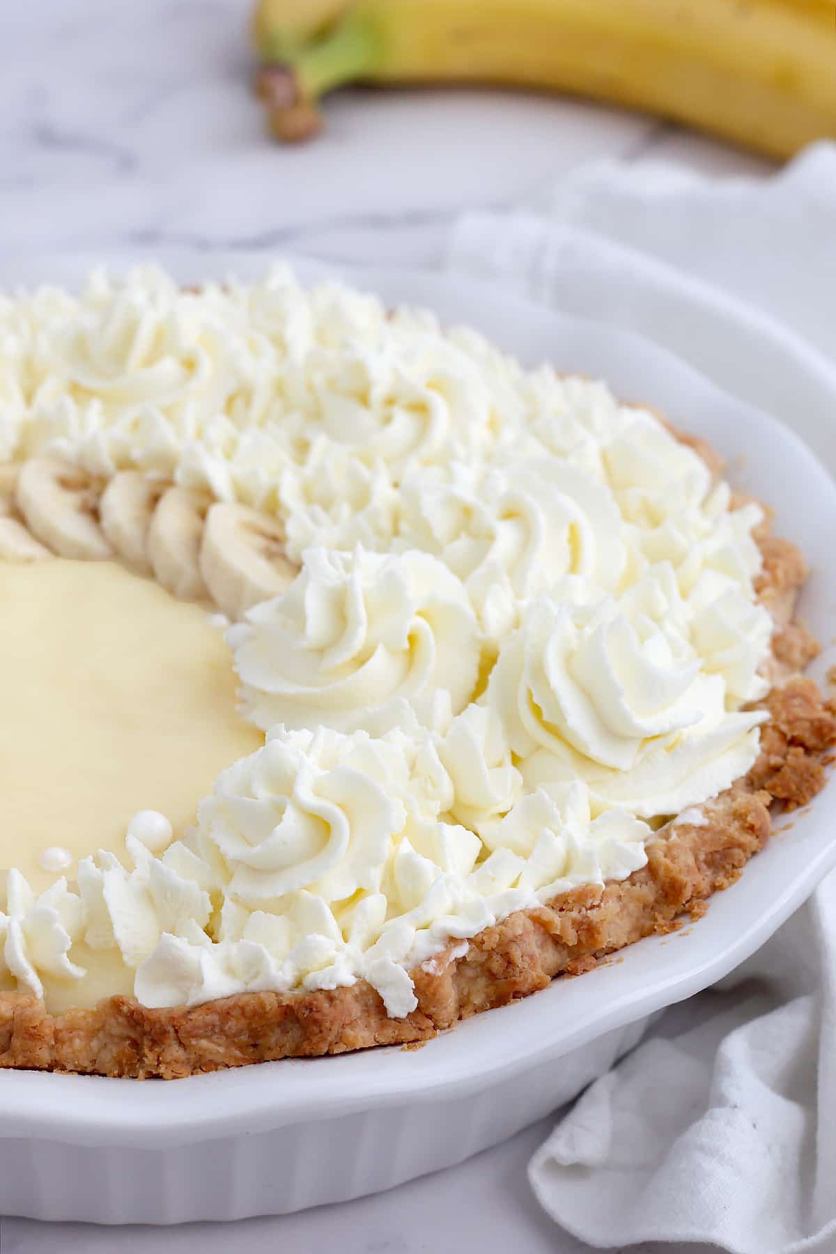 Banana cream pie with a flaky crust topped with swirls of whipped cream and fresh banana slices.