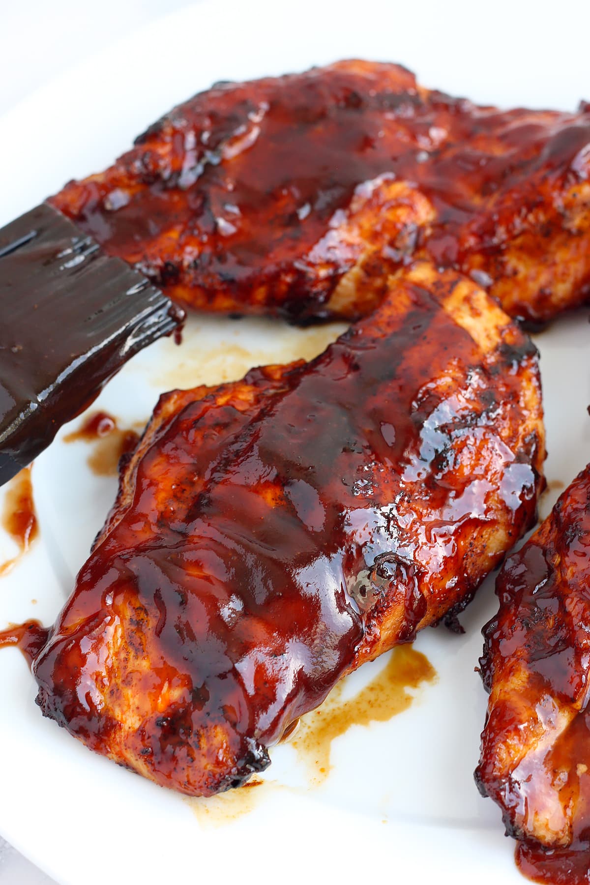 Grilled chicken breasts topped with a smoky barbeque sauce on a serving platter with a pastry brush.