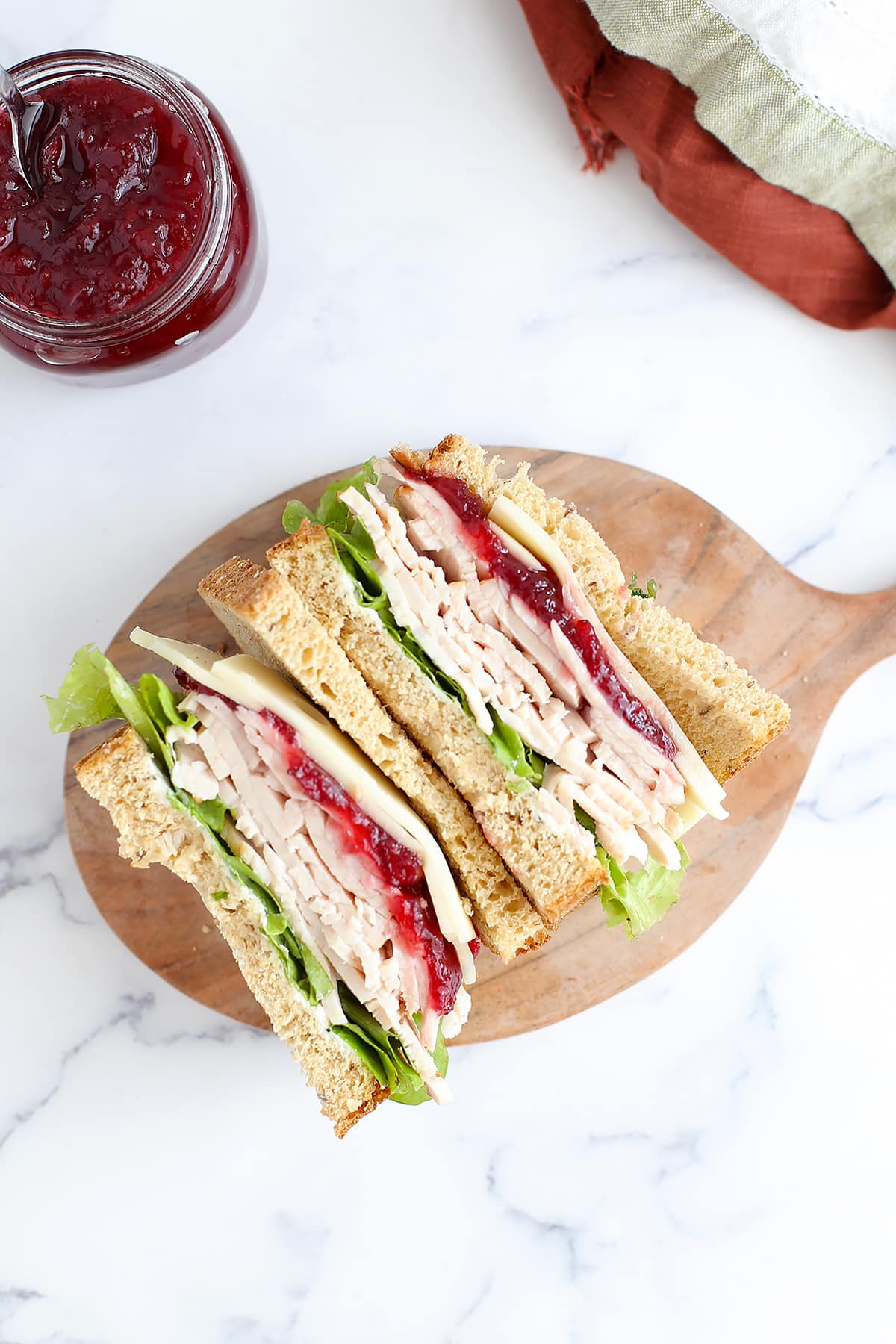 A turkey cranberry sandwich cut in half and placed on a marble counter top with colored linens in the background.