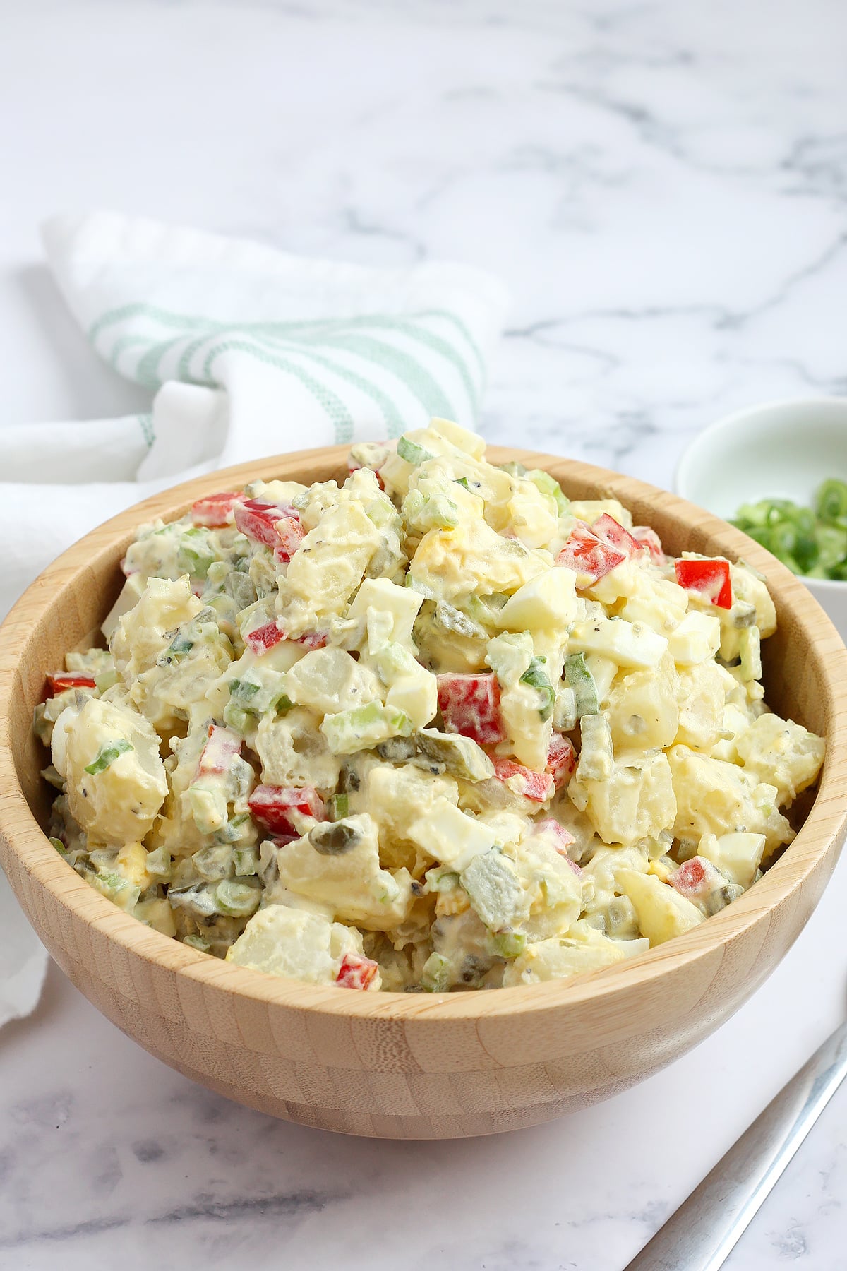 A large wooden serving bowl filled with potato salad with bell peppers, celery, and hard boiled eggs.