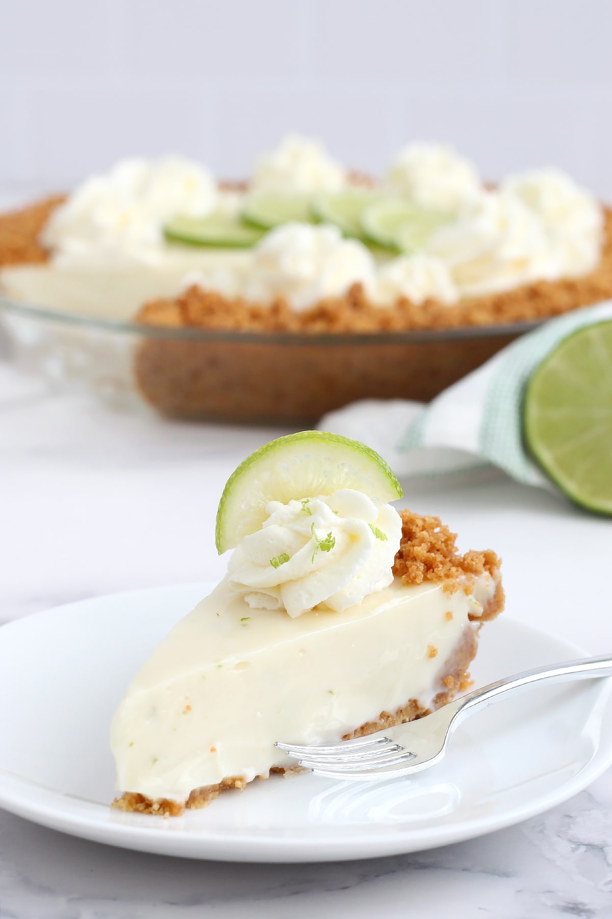 A slice of fresh key lime pie with a graham cracker crust on plate topped with whipped cream and lemon zest