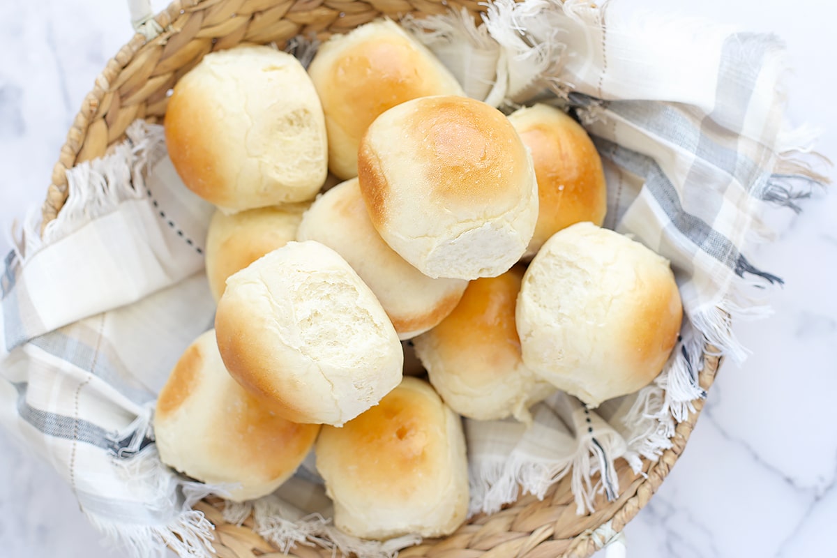 A basket of homemade dinner rolls in with a blue checkered linen. 