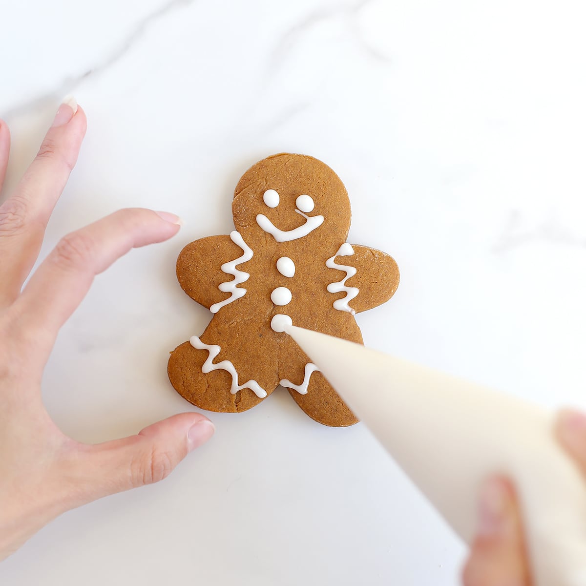 Someone piping icing onto a soft gingerbread cookie man.