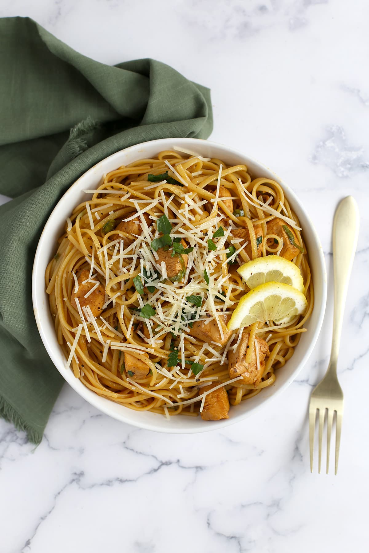 A bowl of insanely good lemon chicken pasta in a white bowl with a green linen in the background.