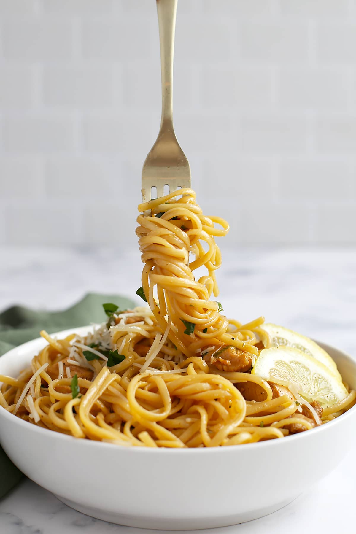 Lemon chicken pasta in a large serving bowl, twisted around a gold fork. 