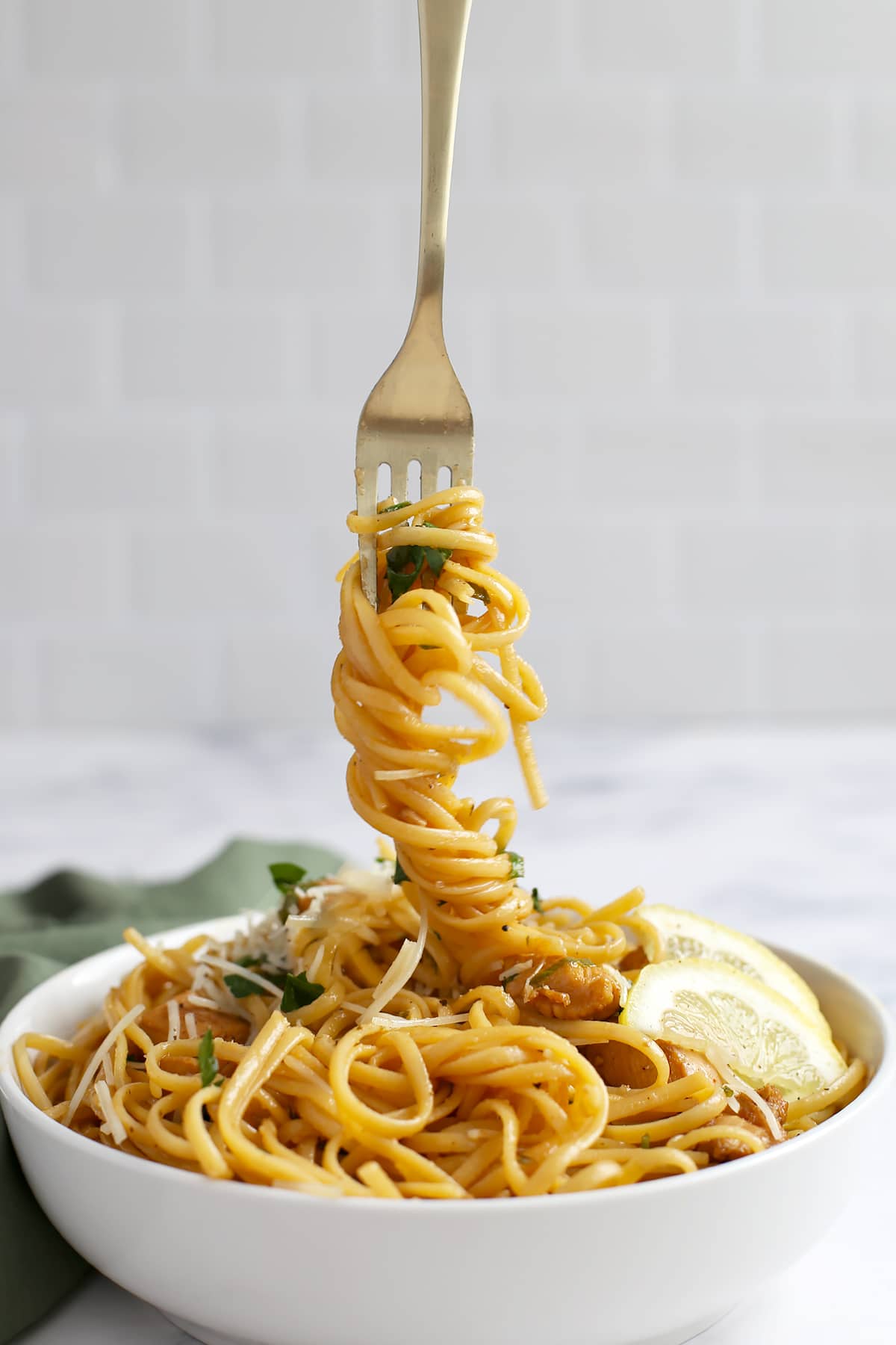 A twirl of pasta noodles on a brass fork being lifted from a bowl of chicken and pasta. 